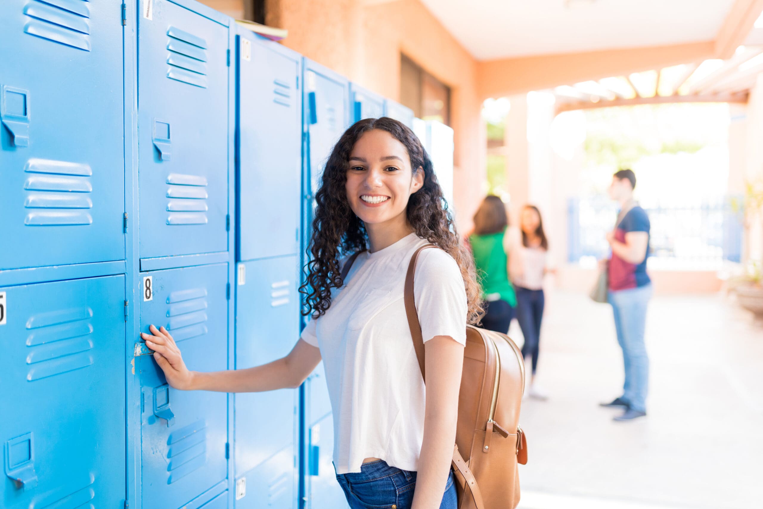Portrait of smiling teenager standing by lockers in high school