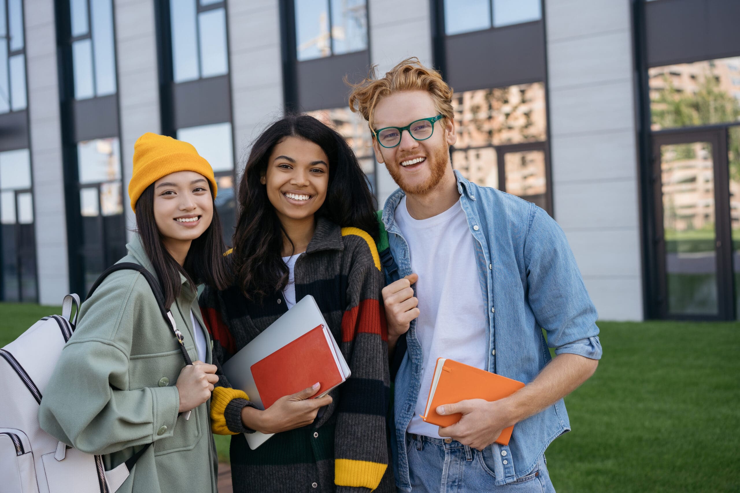 Group portrait of multiracial smiling students with books and backpacks looking at camera walking in university campus.