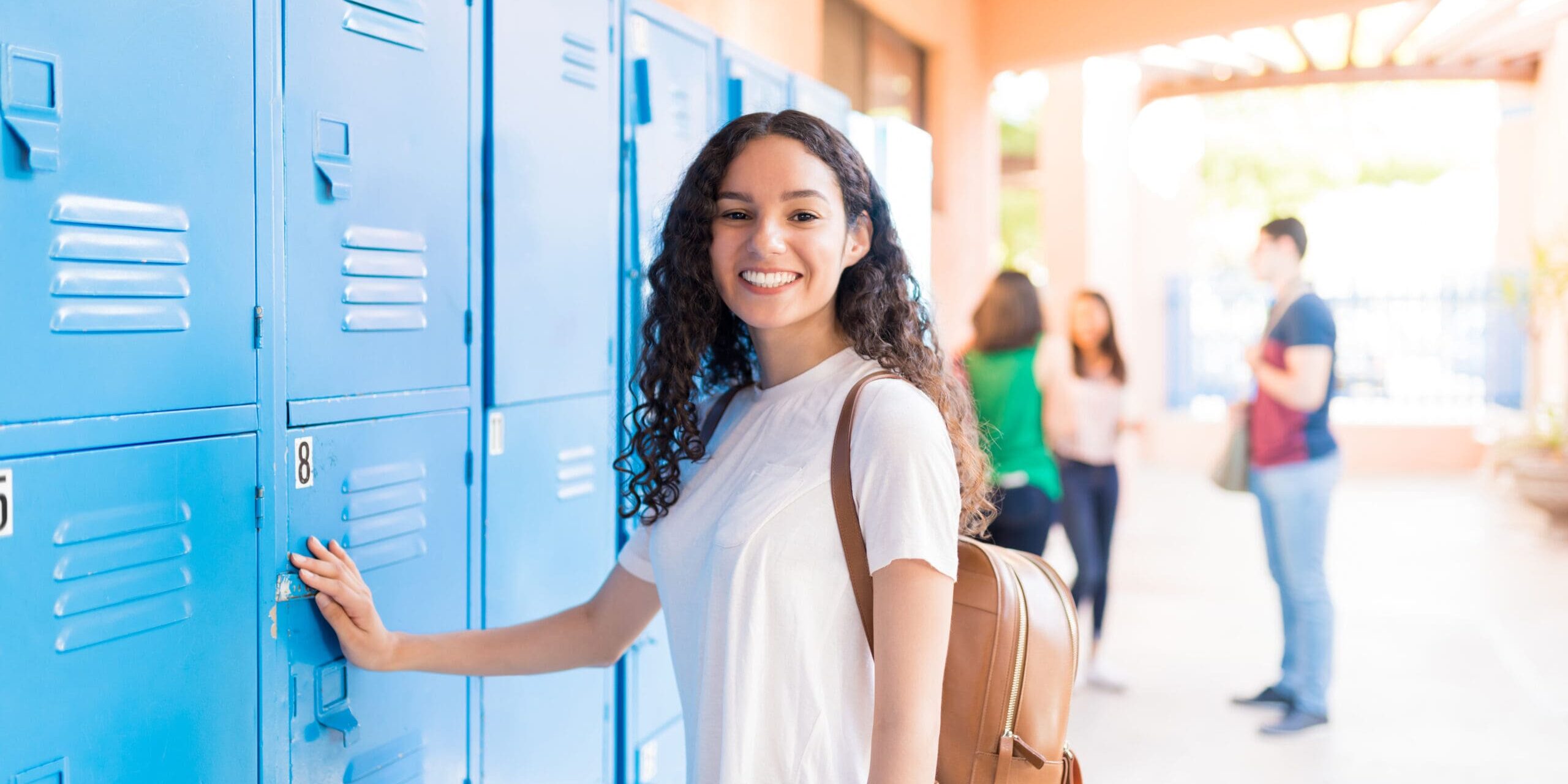 Portrait of smiling teenager standing by lockers in high school