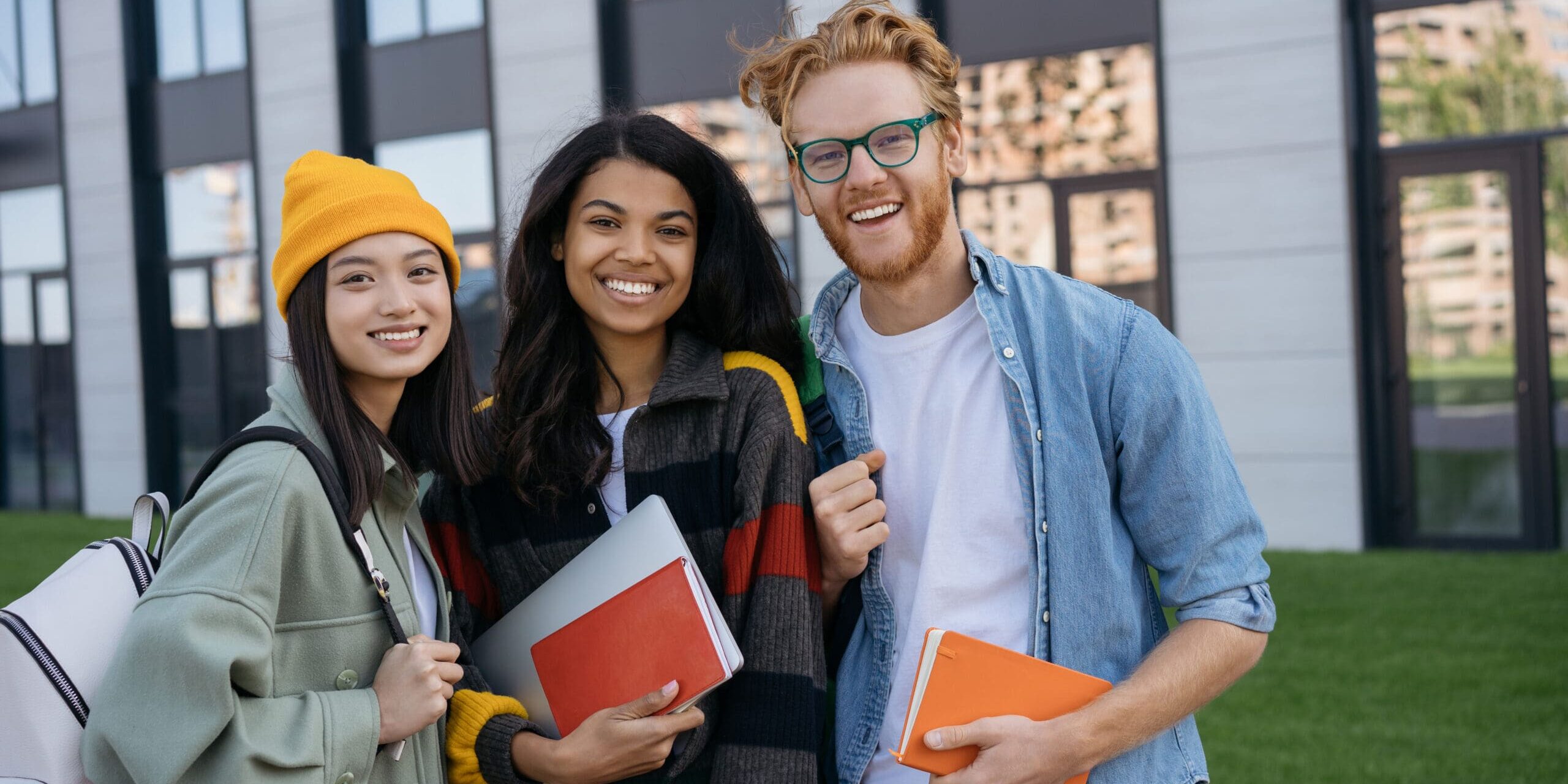 Group portrait of multiracial smiling students with books and backpacks looking at camera walking in university campus.